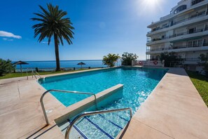 A swimming pool with clear blue water, a palm tree, and a view of the ocean.