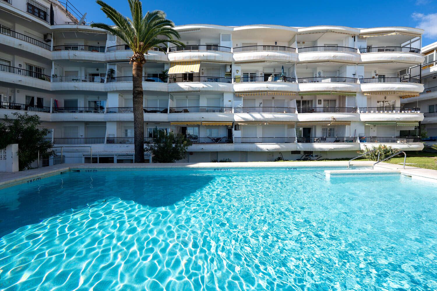 Un hotel de varios pisos con piscina, balcones y palmeras.