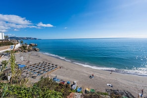 A beach with umbrellas and lounge chairs, a rocky shoreline, and a clear blue sky.