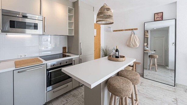 A modern kitchen with white cabinetry, stainless steel appliances, a central island with stools, and a hanging light fixture. - Acapulco Playa 302 by Casasol (Nerja)
