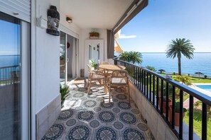 Un balcón con mesa y sillas, vista al mar y piscina.