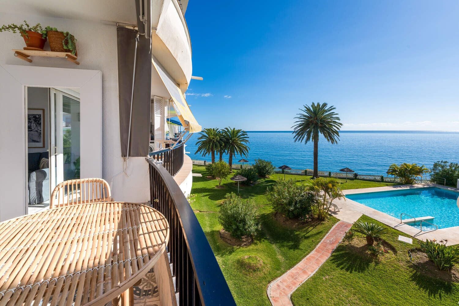Un balcón con vistas al mar, una piscina y un jardín con palmeras.