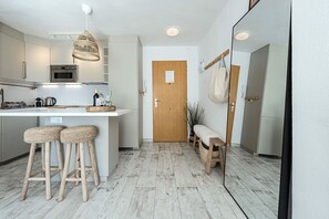 Una cocina moderna con una isla central, taburetes de bar, un banco de madera y una planta colgante.