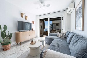 Una sala de estar moderna con un sofá gris, un mueble de madera, un televisor y una planta de cactus.