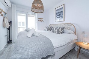 Un dormitorio ordenado con una cama, una mesita de noche, una lámpara colgante y un cuadro en la pared.