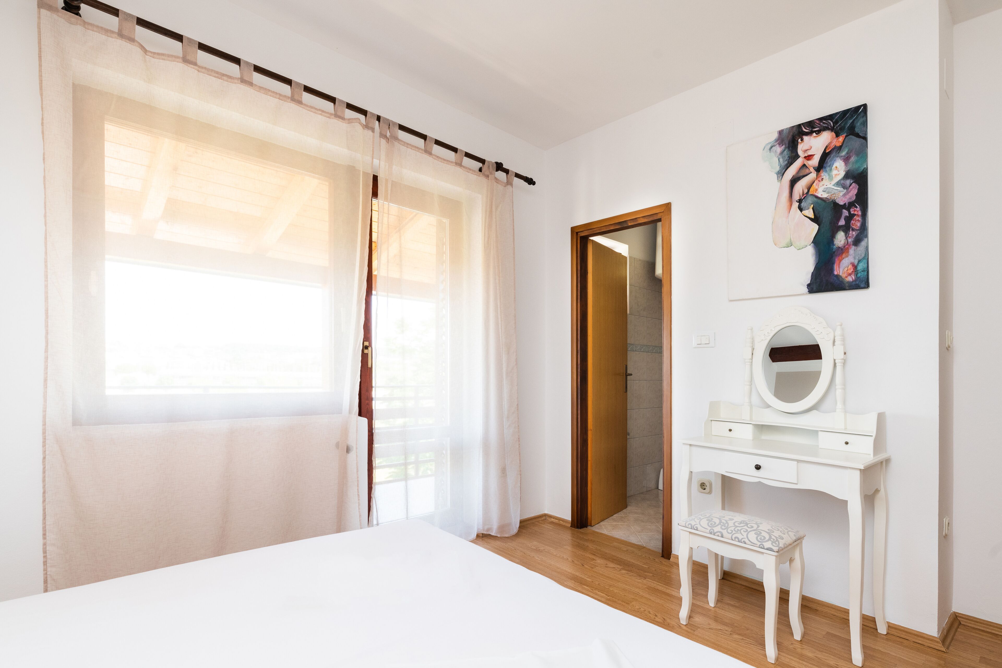 A bedroom with a bed, a vanity with a mirror, and a painting on the wall.