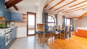 Uma cozinha com armários azuis, uma sala de jantar com mesa e cadeiras, e uma cama com cobertura laranja.