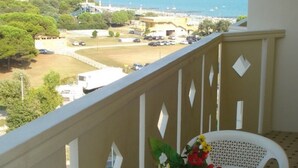 A balcony with a table set for two, overlooking a coastal view with buildings and a clear sky. - Flat with sea view balcony (Porto Santa Margherita)