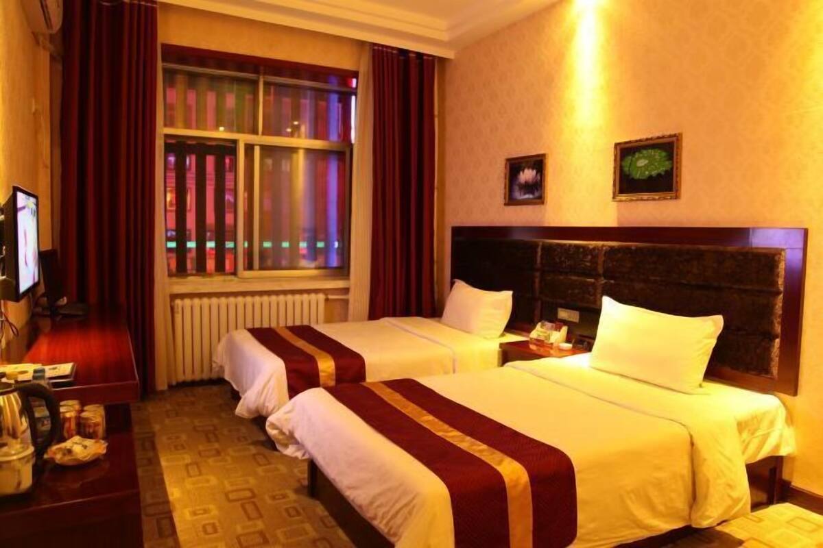 Ein Hotelzimmer mit zwei Betten, einem Schreibtisch mit Computer und einem Fenster mit Vorhängen.