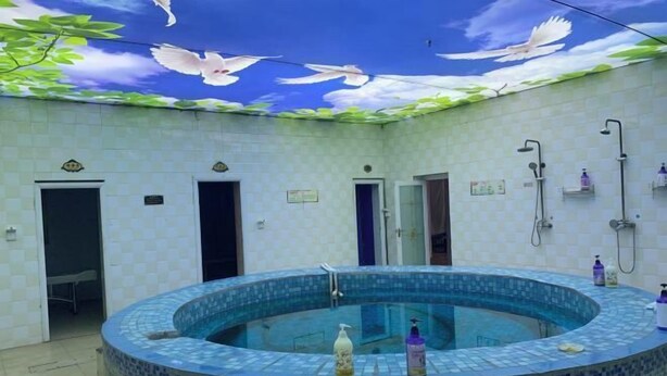 A circular hot tub with mosaic tiles, surrounded by white tiled walls and doors. - Yongchang Lidu Hotel (Yongchang)