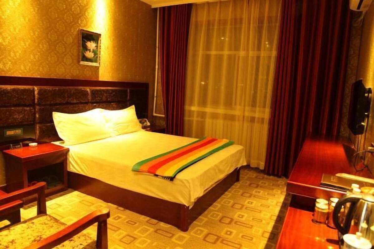Habitación de hotel con cama, mesita de noche, lámpara y vistas al exterior a través de una ventana con cortinas.
