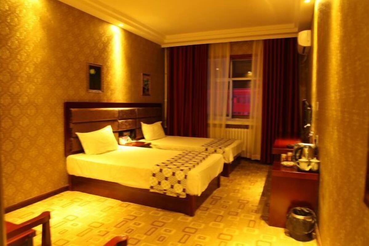 Ein Hotelzimmer mit zwei Betten, einem kleinen Tisch, einem Stuhl und einem Fenster mit Vorhängen.
