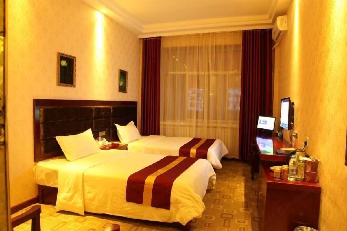Ein Hotelzimmer mit zwei Betten, einem Schreibtisch mit Computer und einem Fenster mit Vorhängen.