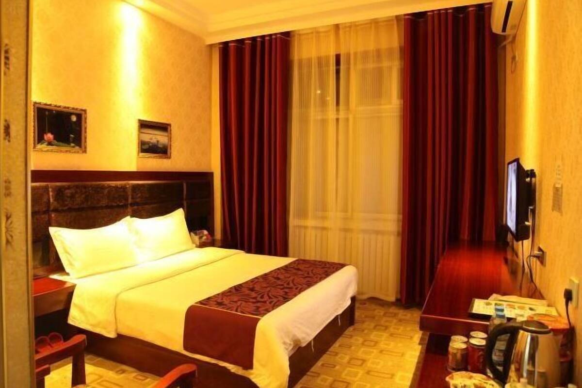 Ein Hotelzimmer mit Bett, Schreibtisch, Stuhl, Fernseher und einem fensterbepflanzten Fenster.