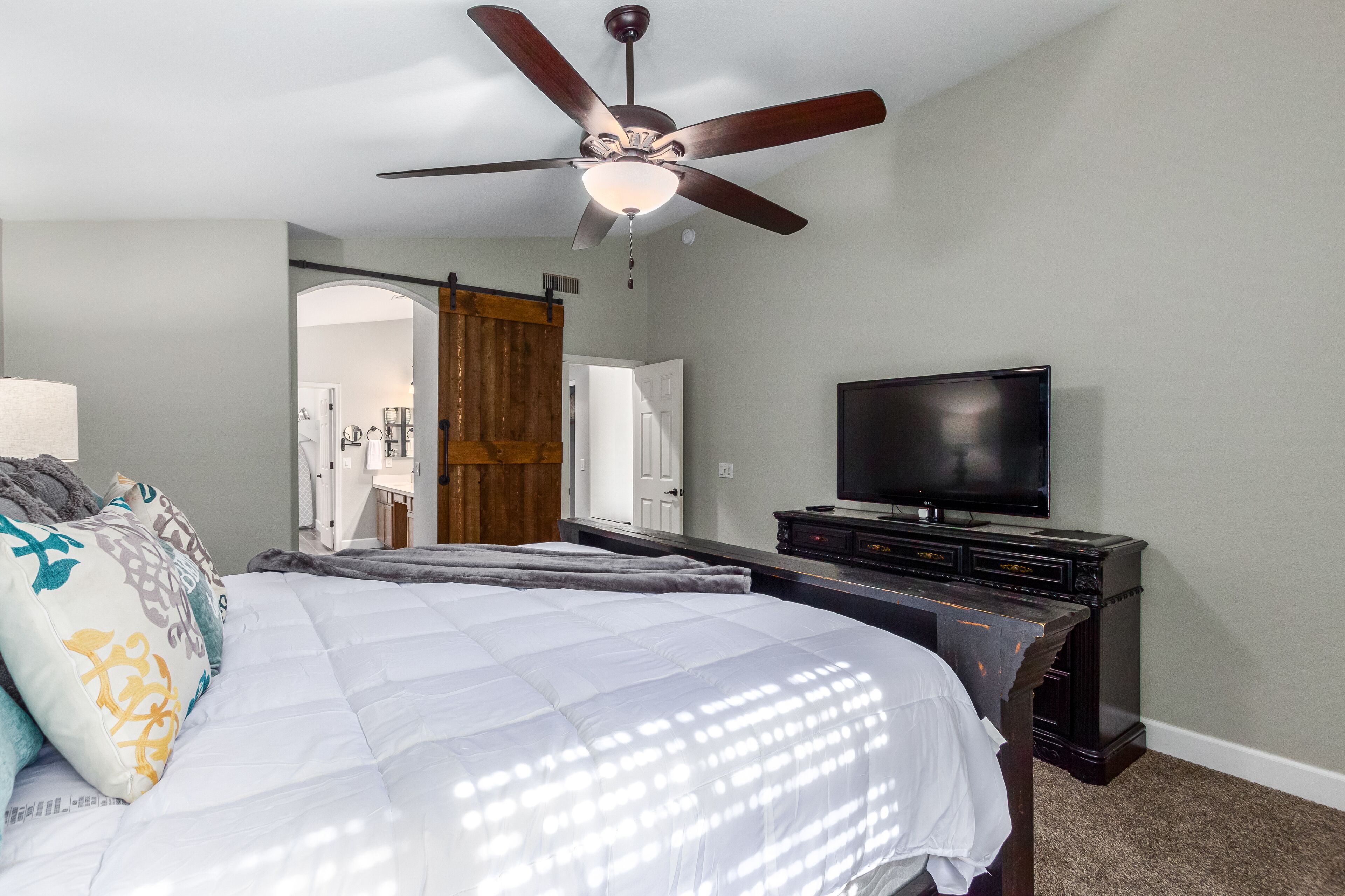 A bedroom with a bed, a ceiling fan, a TV, and a wooden door.