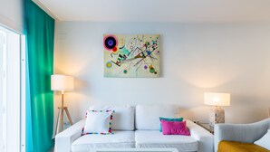 A modern living room with a white sofa, a coffee table, and a colorful abstract painting on the wall. - Ponce Léon. 1-bedroom, private terrace. (Sevilla)