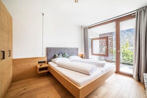 A modern bedroom with a wooden bed, a nightstand, and a large sliding glass door to a balcony.