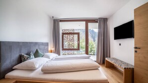 Ein Schlafzimmer mit einem Bett, einer Sitzbank, einem Fernseher und Blick ins Freie.
