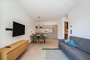 A modern living room with a flat-screen TV, wooden bench, grey sofa, and a kitchen in the background. - Holiday Apartment "Camping Passeier Bergliebe" with Mountain View & Wi-Fi (Saltaus)