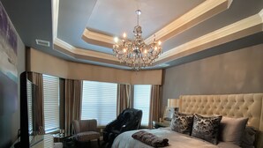 A modern bedroom with a large bed, a chandelier, a desk, and a television. - Newly Listed Oasis (Pearland)