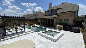 A backyard with a swimming pool, patio furniture, and a covered barbecue area. - Newly Listed Oasis (Pearland)