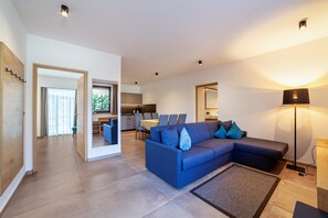 A modern living room with a blue sofa, a dining area, and a kitchen in the background.