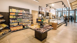 Ein Supermarkt-Innenraum mit Regalen voller verschiedener Produkte, einer zentralen Auslage und Blick durch große Fenster nach draußen.