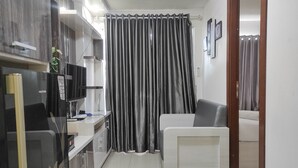 A modern living room with a sofa, a flat-screen TV, and a kitchen area with a refrigerator and cabinets. - Best Deal And Cozy 2Br Vida View Apartment (Makassar)