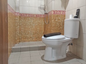 Une salle de bain avec des toilettes, une douche et un sol carrelé.