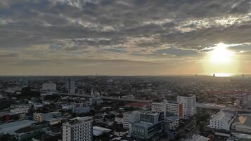 A cityscape with a variety of buildings, including high-rise and low-rise structures, under a partly cloudy sky with the sun setting or rising.