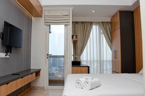 Una habitación de hotel con cama, televisor montado en la pared, escritorio de madera y vistas a la ciudad a través de la ventana.