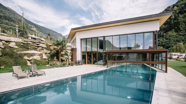 Una casa moderna con piscina, ventanas amplias y vistas a las montañas.