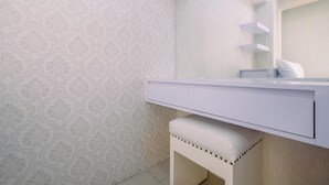 A bathroom with a patterned wallpaper, a white vanity with a mirror, and a bench. - Simple And Cozy Living 2Br At Cibubur Village Apartment (Depok)