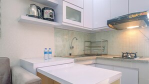 A compact kitchen with white cabinetry, a microwave, a kettle, and a gas stove. - Simple And Cozy Living 2Br At Cibubur Village Apartment (Depok)