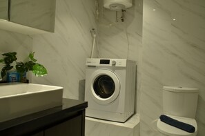 Bathroom features a washing machine, sink, and toilet, with a potted plant on the countertop.