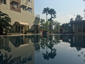 A modern building with a swimming pool reflecting the surrounding trees and architecture. - Cozy 2Br At Pinewood Apartment (Cileunyi)