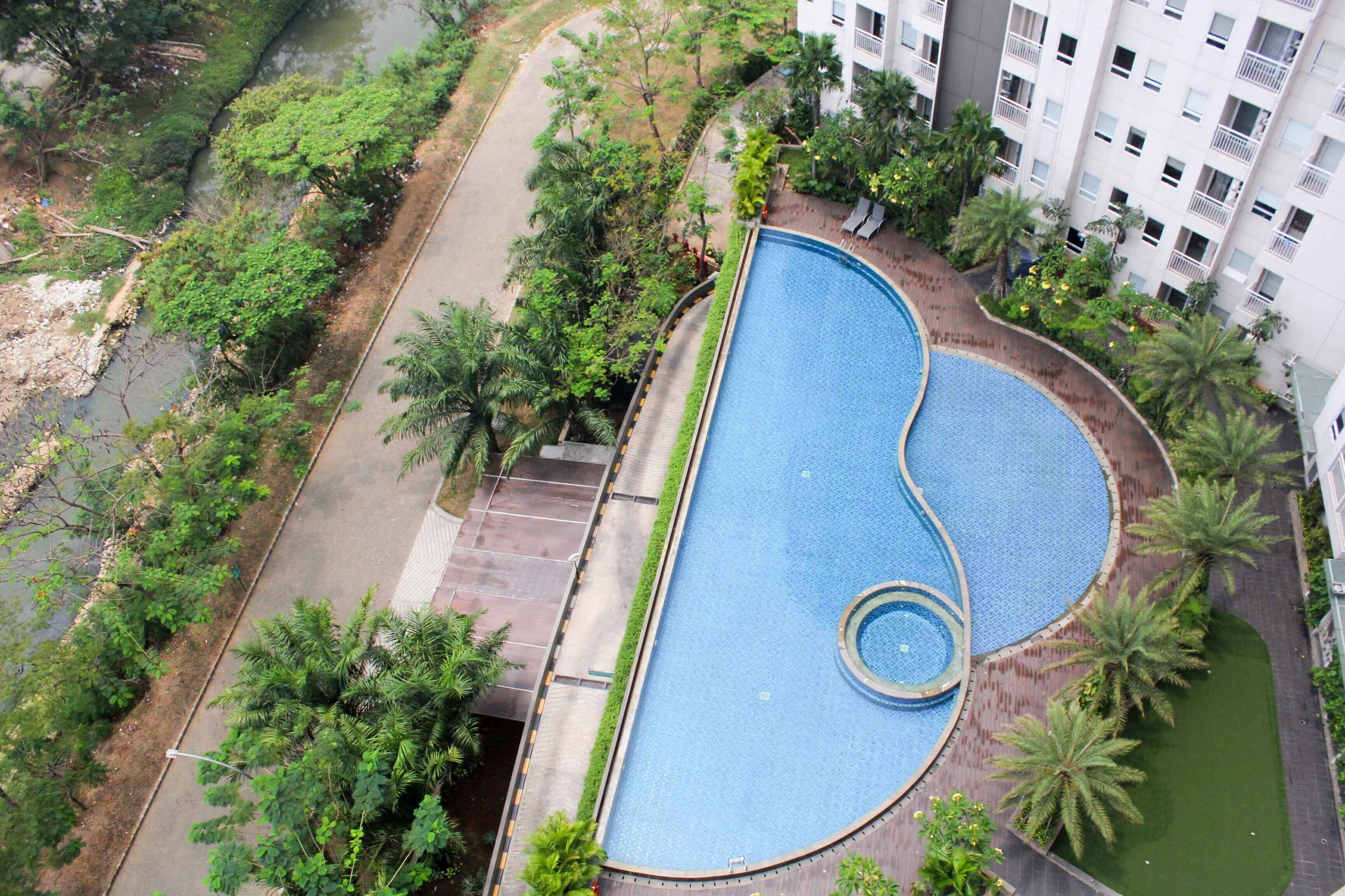 Une vue aérienne d’une piscine entourée de verdure, située à côté d’un immeuble à plusieurs étages.