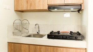 A kitchen with wooden cabinets, a stainless steel sink, a dish rack, and a gas stove. - Comfortable 2Br Apartment At Mustika Golf Residence (Cikarang)
