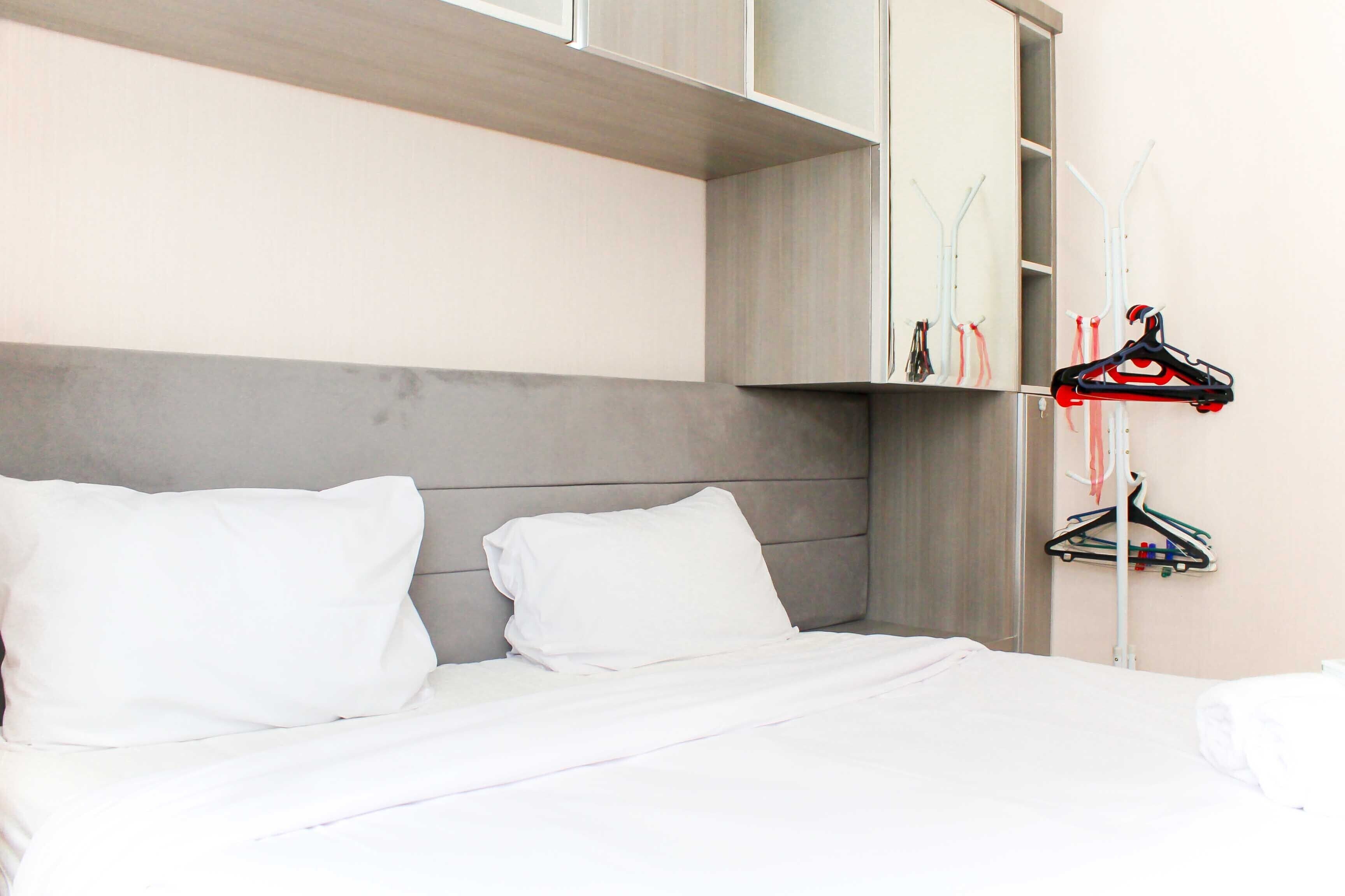 A neatly made bed with white linens, a grey headboard, and a wall-mounted clothing rack with hangers.