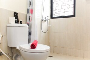 Une salle de bain comprenant des toilettes, une douche et une fenêtre ornée d’un motif géométrique.