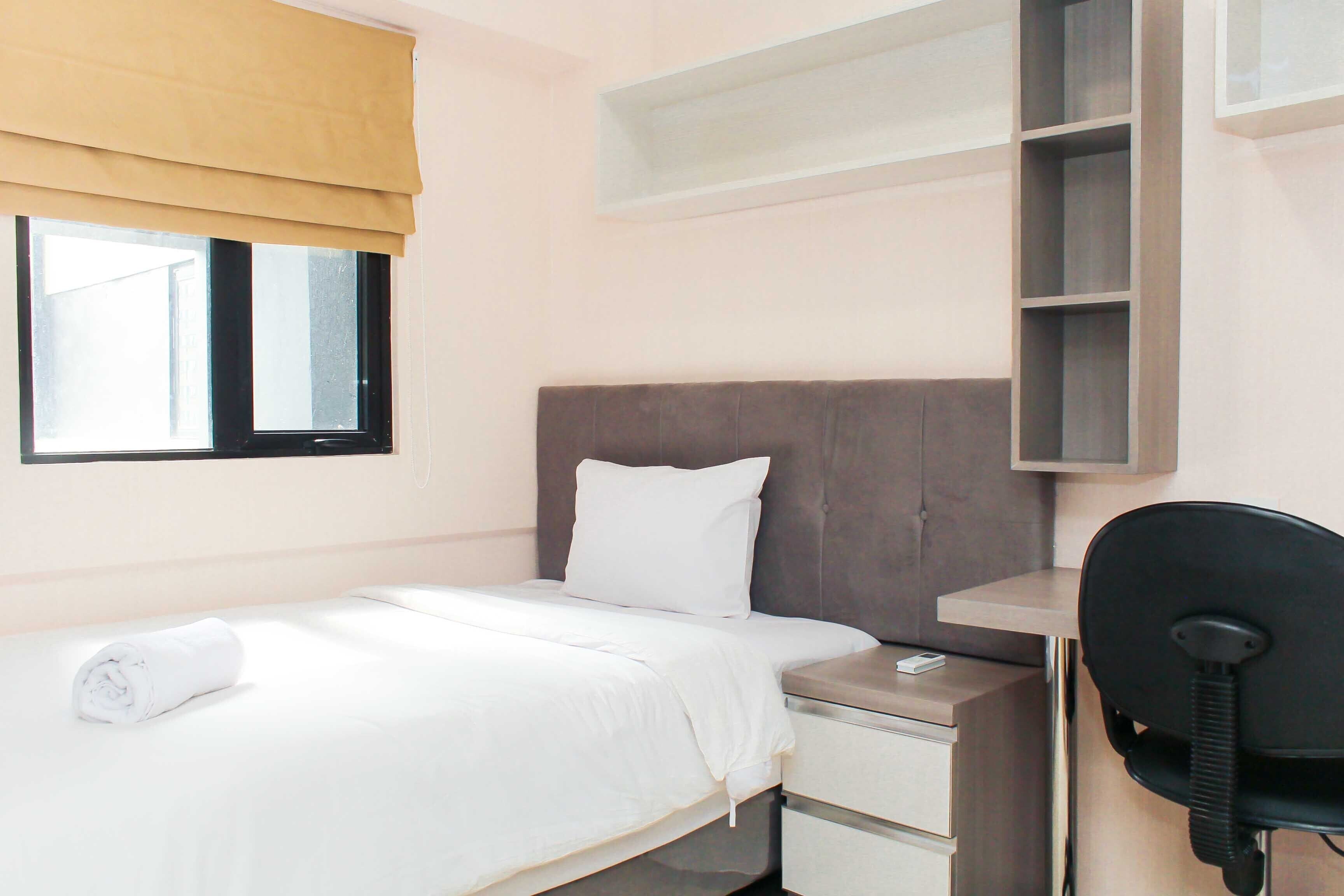 A neatly made bed with white linens, a bedside table with a phone, and a desk with a chair.