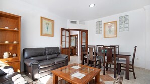 Un salon comprenant un canapé en cuir, une table basse avec un plateau en verre, une table à manger en bois avec des chaises, et un tapis à motifs.