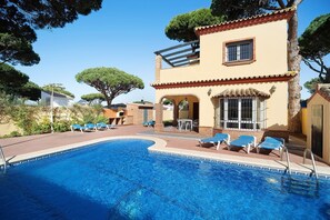 Una piscina con sillas de descanso, un patio y un edificio con techo de tejas y ventanas arqueadas.