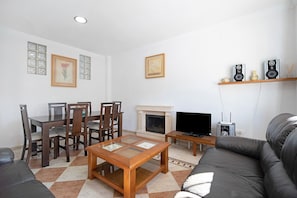 Una sala de estar con chimenea, televisor, sofá, mesa de comedor con sillas y cuadros en la pared.