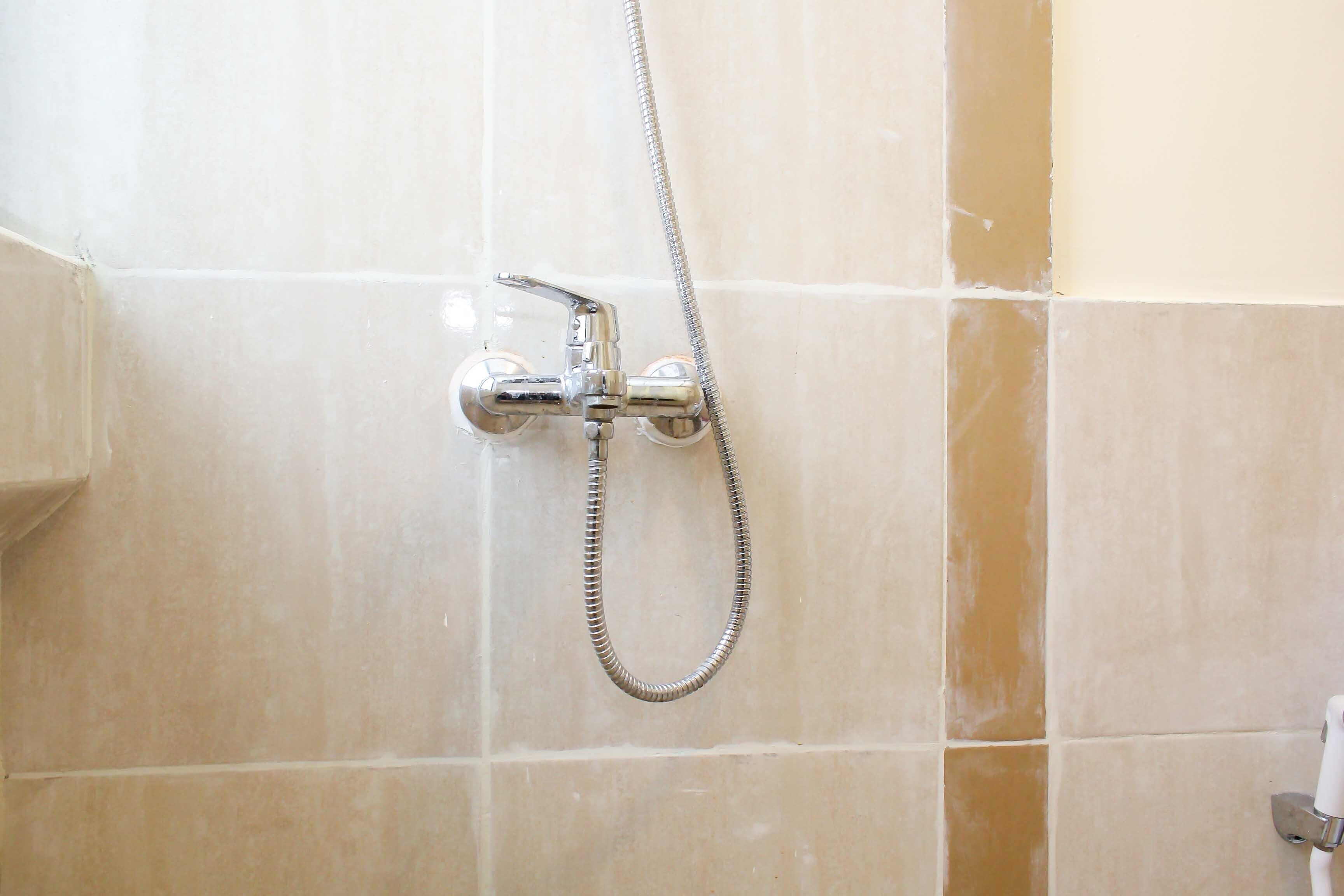Um chuveiro com um chuveiro manual e um chuveiro fixo, instalado numa parede revestida de azulejos.