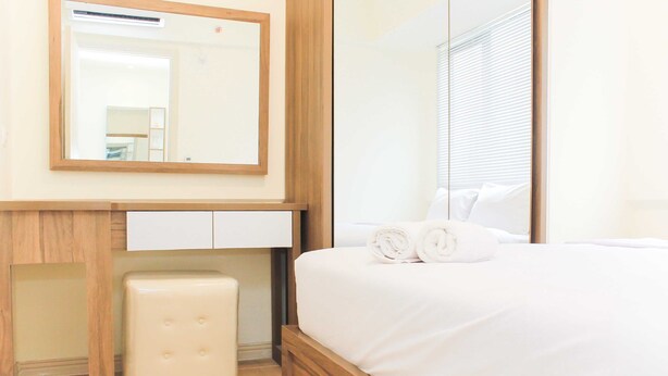 Una habitación de hotel con un marco de cama de madera, una mesita de noche blanca, un espejo y un taburete blanco pequeño.