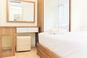 A hotel room with a wooden bed frame, a white bedside table, a mirror, and a small white stool.
