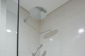 Una ducha con un cabezal de ducha de mano y un cabezal de ducha redondo en el techo, en un baño con azulejos.