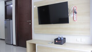Une chambre d’hôtel moderne dotée d’un téléviseur à écran plat fixé au mur, d’un minibar et d’une porte avec une poignée.