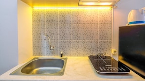 A kitchen with a sink, a microwave, and a tiled backsplash. - Good Deal Studio At Evenciio Apartment Margonda Near Ui (Depok)